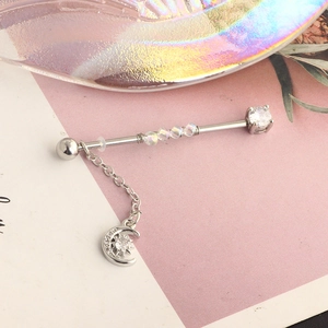 Detail of industrial barbell earring with moon and sun chain pendants and cubic zirconia