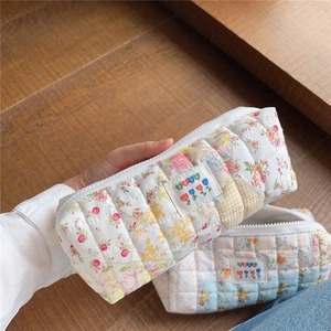 Handheld view showing quilted floral cotton texture and zipper detail of the makeup bag