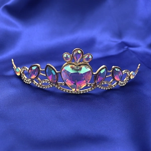 Close-up of golden princess crown featuring a large heart-shaped crystal on blue silk