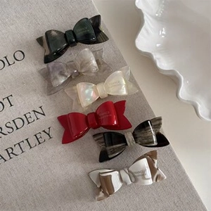 Detailed set of six acetate bow hair clips in various marble and solid colors on a book