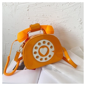 Close-up of vintage rotary phone crossbody bag in glossy bright orange patent leather