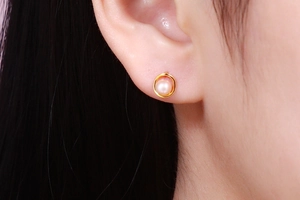 Macro view of dainty 925 silver pearl stud earring with golden circular hollow frame