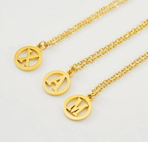 Détail de trois colliers en acier inoxydable doré 18K avec pendentifs lettres X, A et M