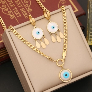 Golden evil eye jewelry set with shell pendant and tassel earrings on leather box