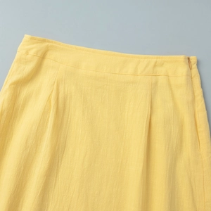 Detail view of yellow skirt featuring hidden side zipper and pleated waistline design