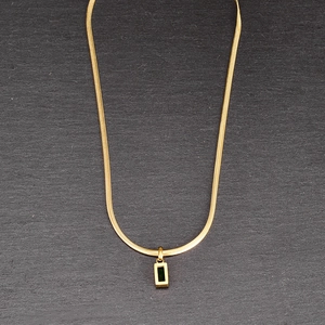 Macro view of gold snake chain with emerald cut black stone pendant on stone texture
