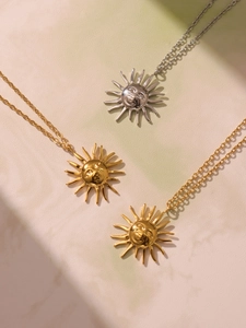 Three sun face necklaces in gold and silver finish on a natural textured surface