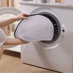 Close-up of a white mesh laundry bag with black trim being placed into a washing machine