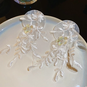 Gros plan de boucles d'oreilles en dentelle blanche avec fleurs en résine irisée