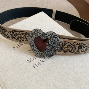 Detail of vintage heart buckle with red gemstone and rose embossing on floral leather belt