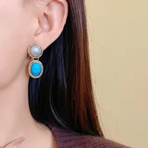 Vintage gold drop earrings with white pearl and oval turquoise stones on a model