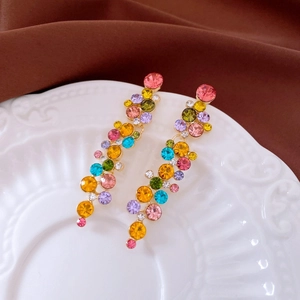 Close-up of colorful rhinestone tassel earrings on a vintage white embossed plate