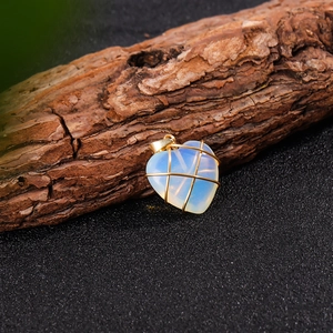 Dettaglio di un ciondolo a cuore in opale avvolto in elegante filo d'oro su ramo