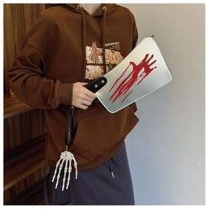Detail of cleaver-shaped crossbody bag with red bloody handprint and skull pendant