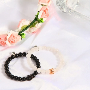 Close-up of magnetic couple bracelets with crown charms and matte stone beads on white silk