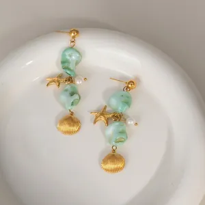 Detailed view of gold starfish and shell pendants with green beads on a white plate