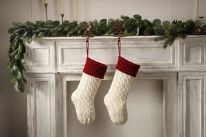 Close-up of white knitted Christmas stockings with red cuffs hanging on a fireplace