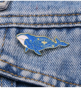 Macro shot of blue enamel whale brooch with celestial galaxy patterns on denim fabric