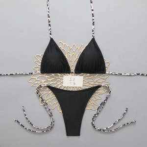 Detail of black bikini set featuring leopard print straps on a decorative gold mat