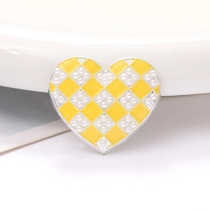 Detailed view of heart-shaped charm with yellow checkerboard pattern and pearl inlay