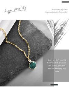Macro view of gold necklace featuring a round green malachite pendant and small white crystal