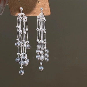 Detailed view of silver-toned long tassel earrings with metallic bead accents on card