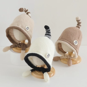 Close-up of baby winter knit earflap hats in three neutral colors with unique tail tops