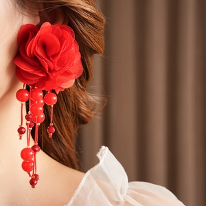 Gros plan de boucles d'oreilles fleurs en tissu rouge avec pompons en perles sur un mannequin