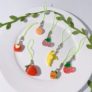 Detailed view of colorful resin fruit phone charms with green cords on white ceramic plate