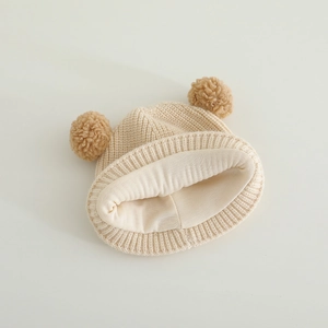 Close-up of baby knit hat with plush double pom-poms and warm fleece lining texture