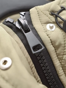Detail of olive green quilted fabric with black zipper and silver metal snap button