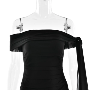 Détail de robe moulante noire à épaules dénudées avec ruban latéral et tissu drapé