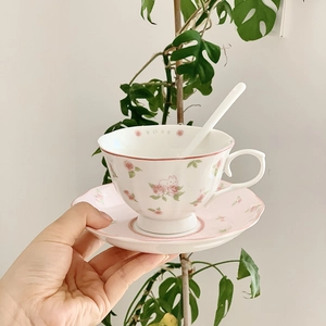 Close-up of ceramic coffee cup and saucer with pink rose and cat pattern and spoon