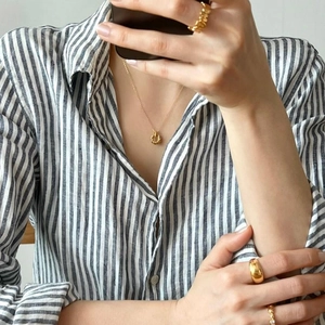 Model wearing a gold twist rope necklace and stacked textured rings with striped shirt