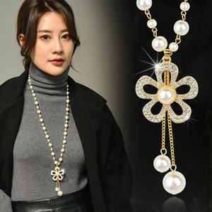 Detail of long pearl sweater chain featuring a gold floral pendant with rhinestones