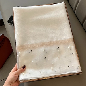White silk shawl with gold tulle trim and elegant pearl bead accents on a leather background