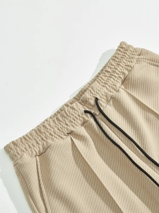 Detail of khaki corduroy trousers featuring elastic waistband and black drawstring texture