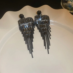 Detailed macro shot of long gun-black tassel earrings with black rhinestones on white plate