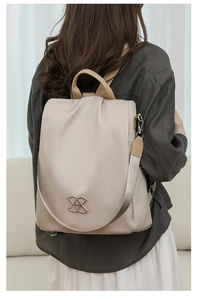 Rear view of a model wearing a beige waterproof nylon backpack in a home setting