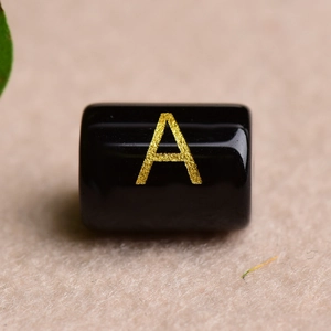 Macro shot of a polished black rectangular bead featuring a gold-toned letter A engraving