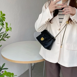 Close-up of black quilted chain bag with metal clasp styled with a white blazer
