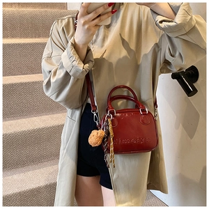 Detail of red glossy handbag featuring embossed letters and a cute plush bear pendant