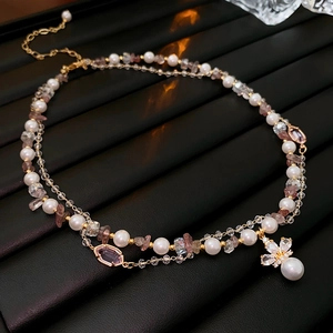 Detail of a double-layered gold necklace with pearls, pink stones and floral pendant