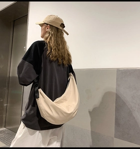 Rear view of model wearing a large beige nylon crescent crossbody bag in urban setting