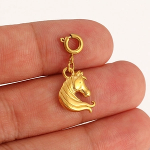 Macro view of a gold-plated horse head pendant held by a hand to show actual size