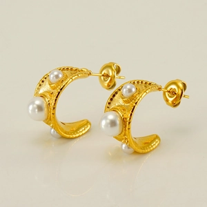 Détail macro de boucles d'oreilles C dorées avec perles blanches sur fond clair