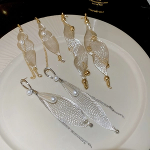 Detail view of mesh leaf earrings with pearls and tassels on a white ceramic plate
