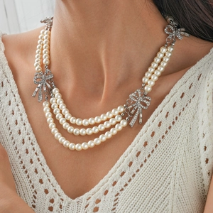 Detail of multi-layer pearl necklace featuring three silver bows with sparkling crystals