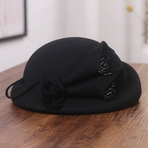 Détail d'un chapeau bibi noir en feutre de laine avec fleur en tissu et pompons perlés