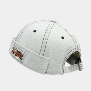 Detail of light blue denim skullcap with leopard patch and red cursive embroidery